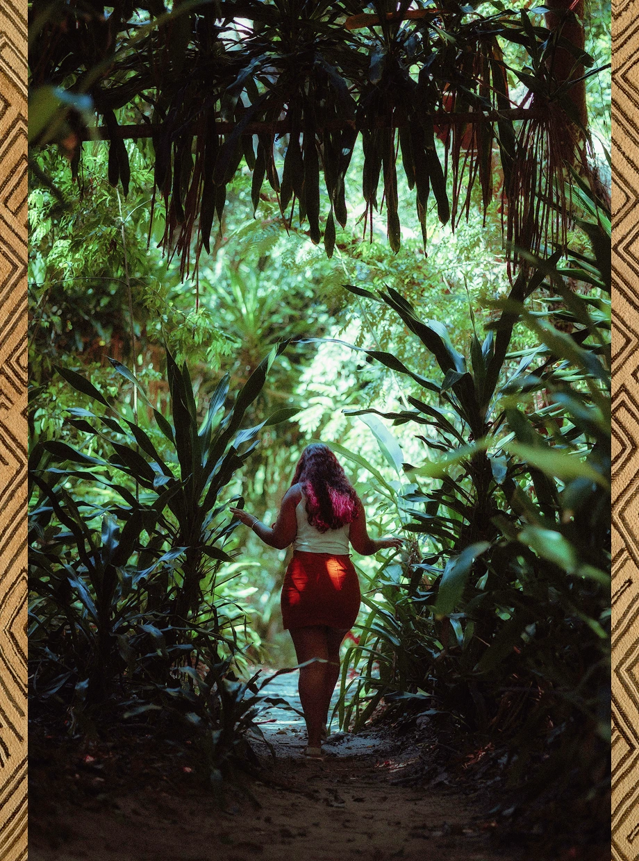 Woman in a red skirt and white top walking through a lush, green tropical forest path.