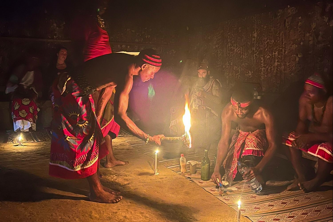 Men in traditional attire performing a nighttime fire ritual indoors with candles and bottles.