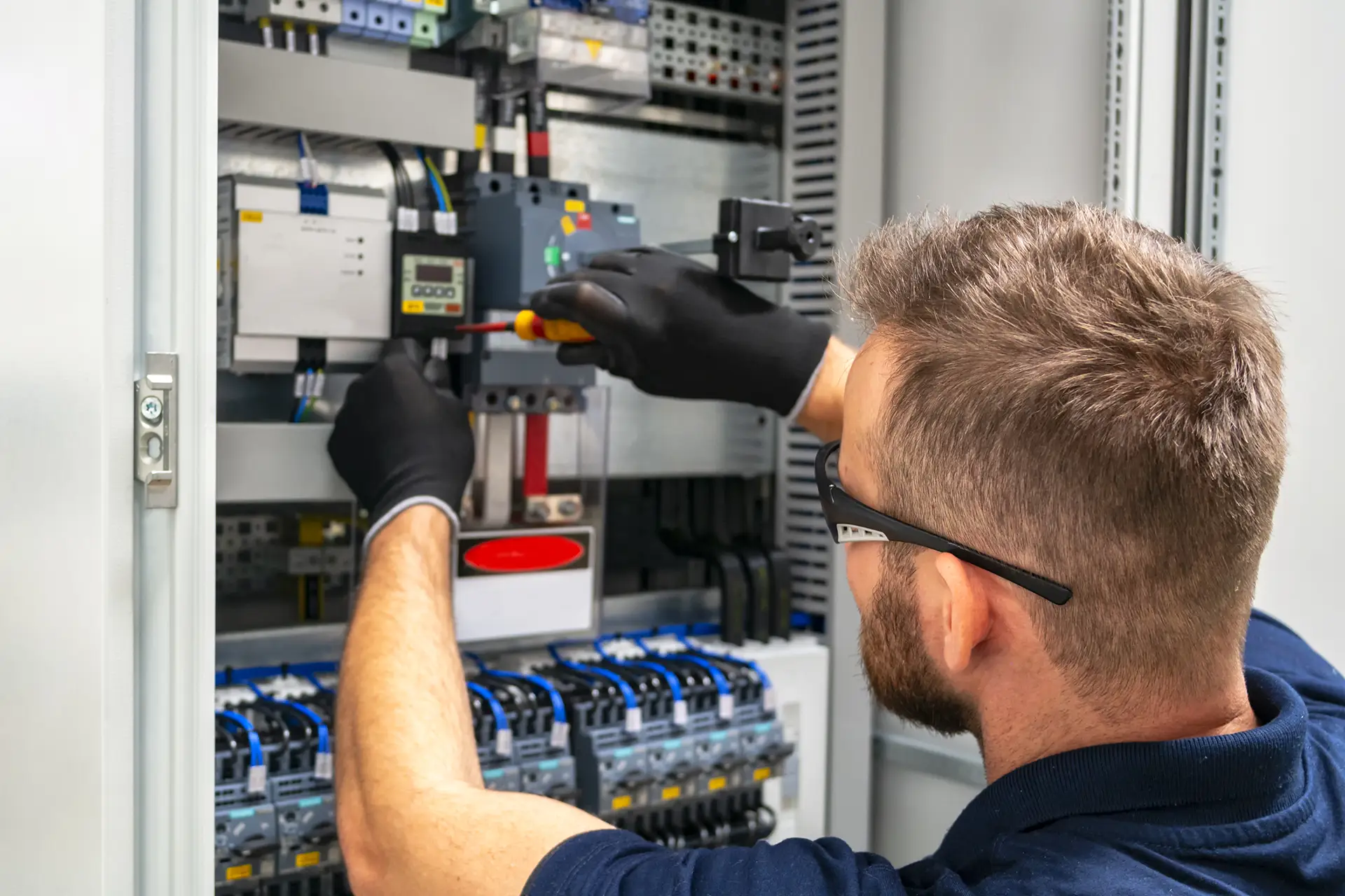 A service technician working inside an electrical cabinet, following guidance on a tablet