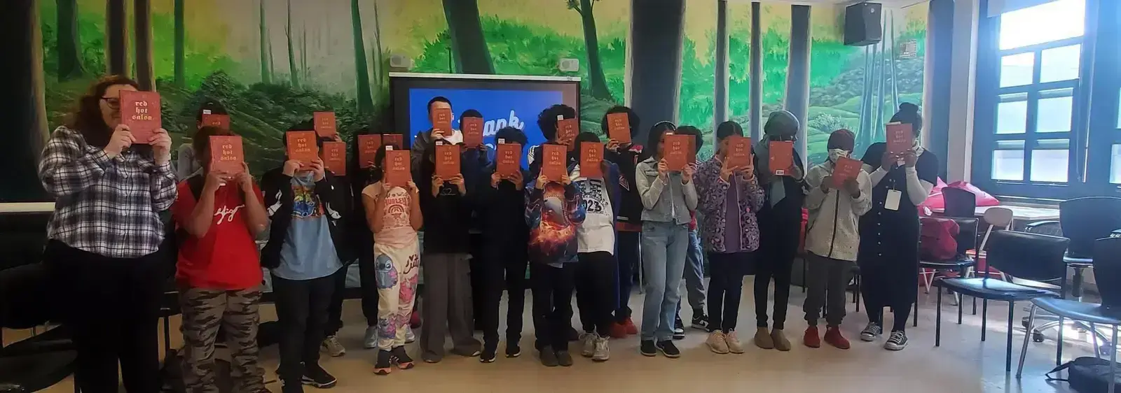 Students and teacher holding up matching red books in classroom