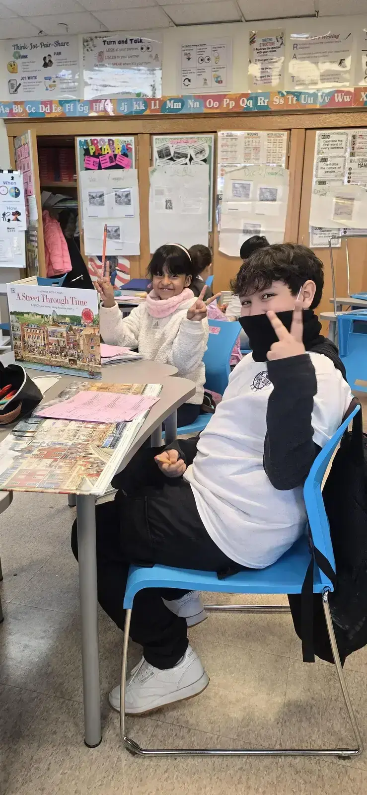 Two students smile and gesture peace signs at classroom desks