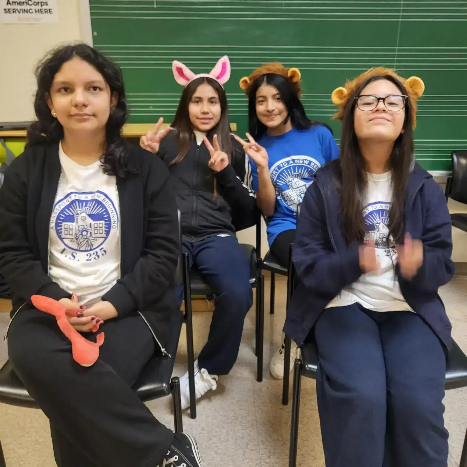 Four IS 235 students wearing school shirts and fun animal headbands in classroom