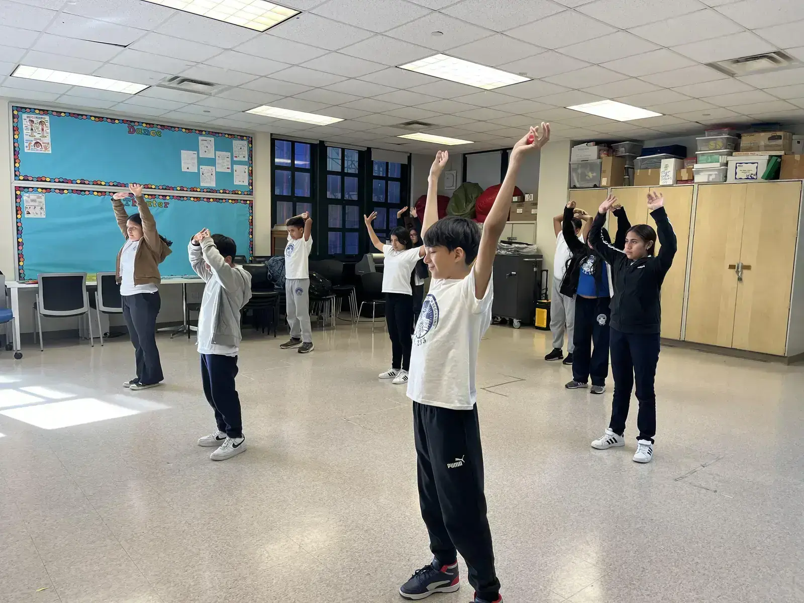 Students raising arms during dance or movement class with teacher