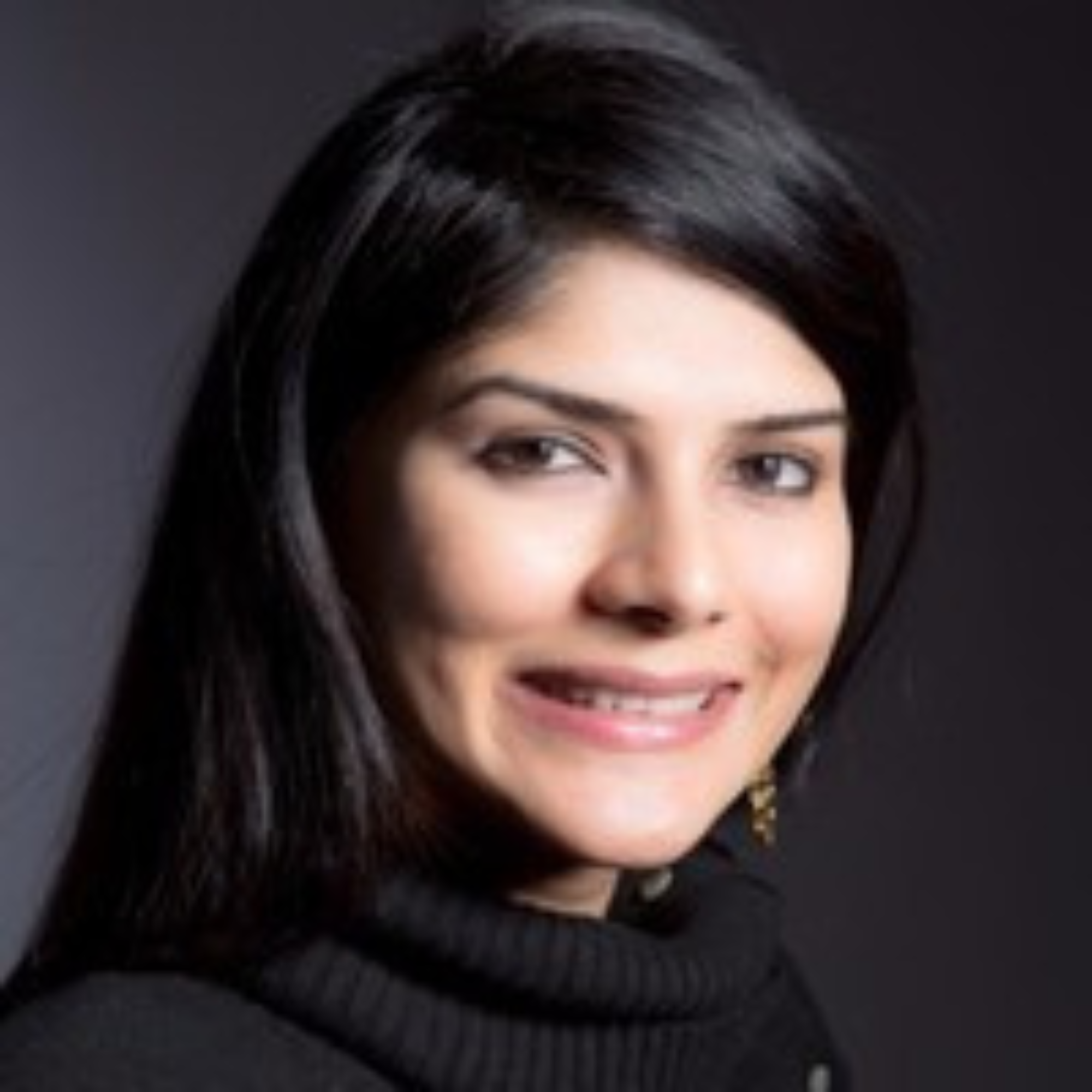 Smiling woman with long dark hair wearing gold earrings and a black turtleneck sweater.