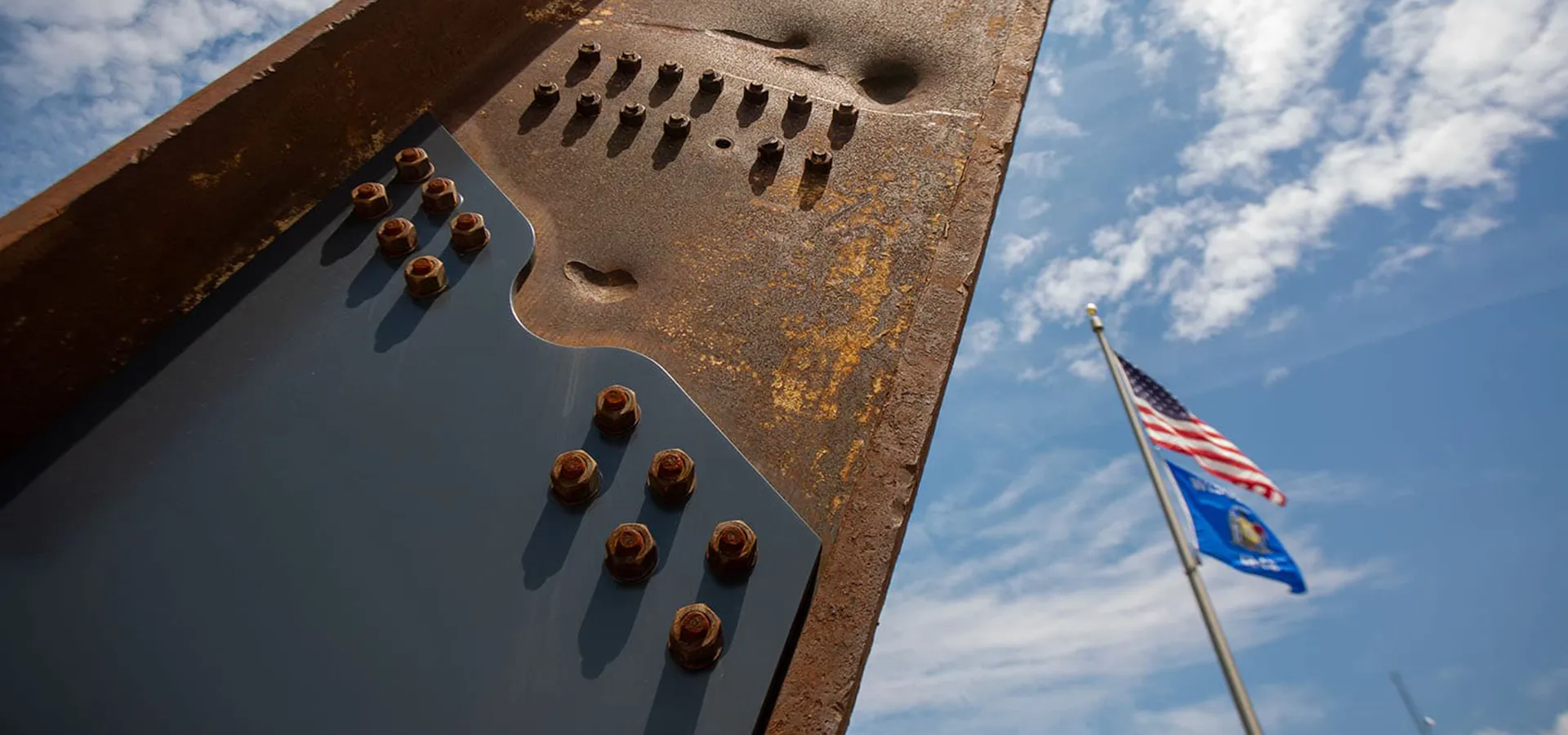 The steel beam at the Memorial with the American and Wisconsin flags flying behind.