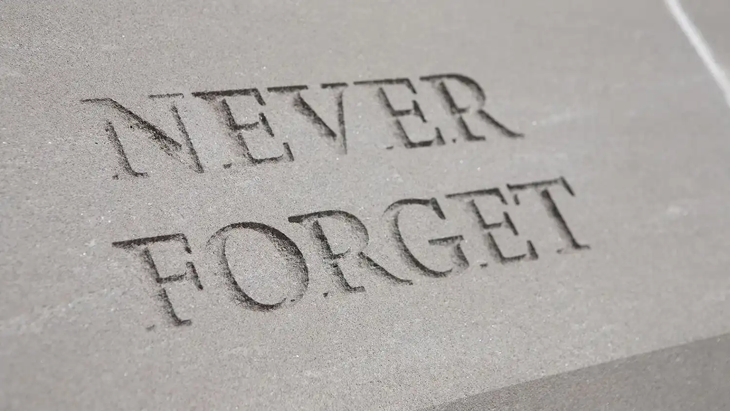 Gray stone surface engraved with the words Never Forget in capital letters.