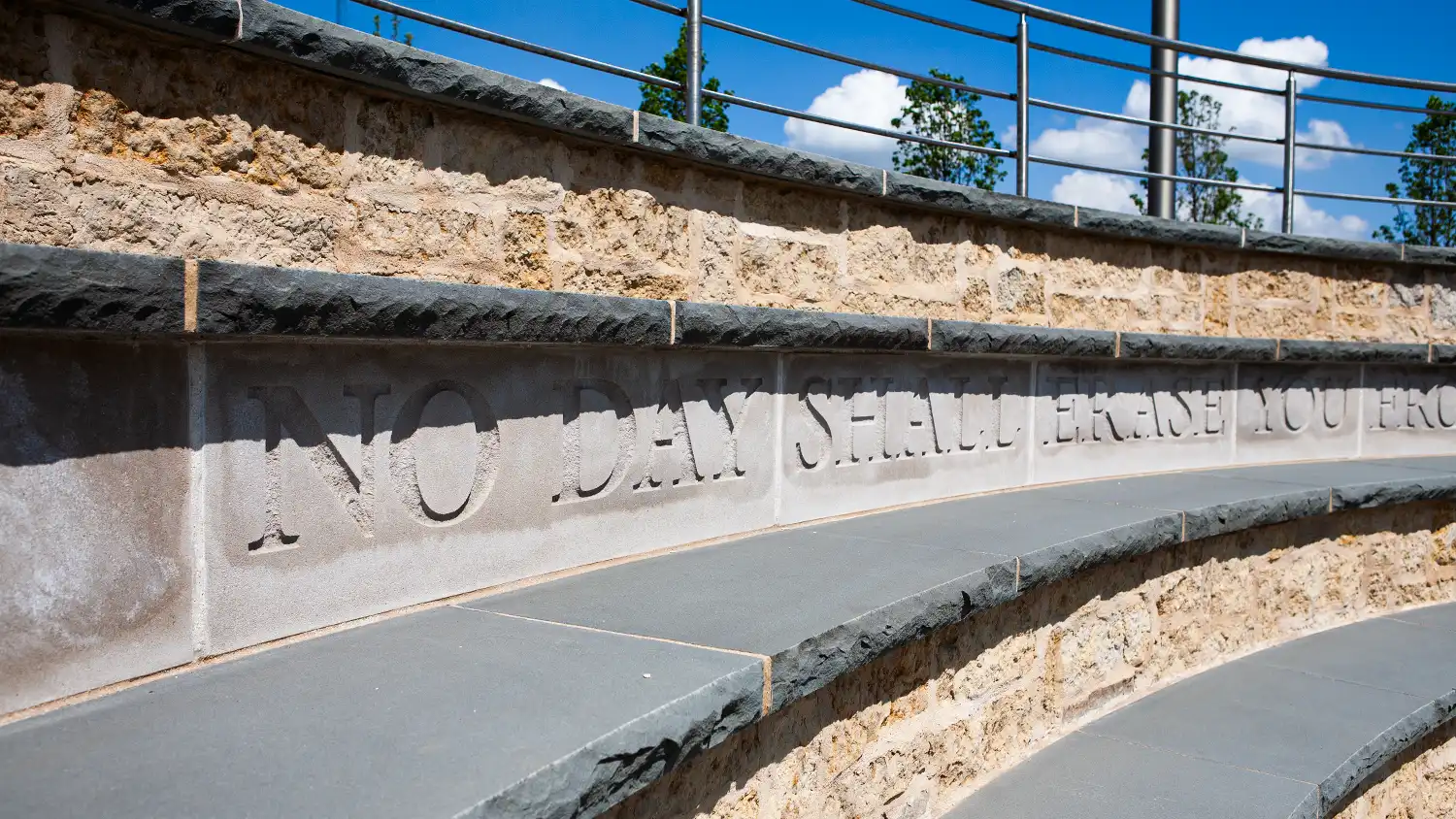 Curved stone steps with an inscription partially reading, 'NO DAY SHALL ERASE YOU' under a railing.