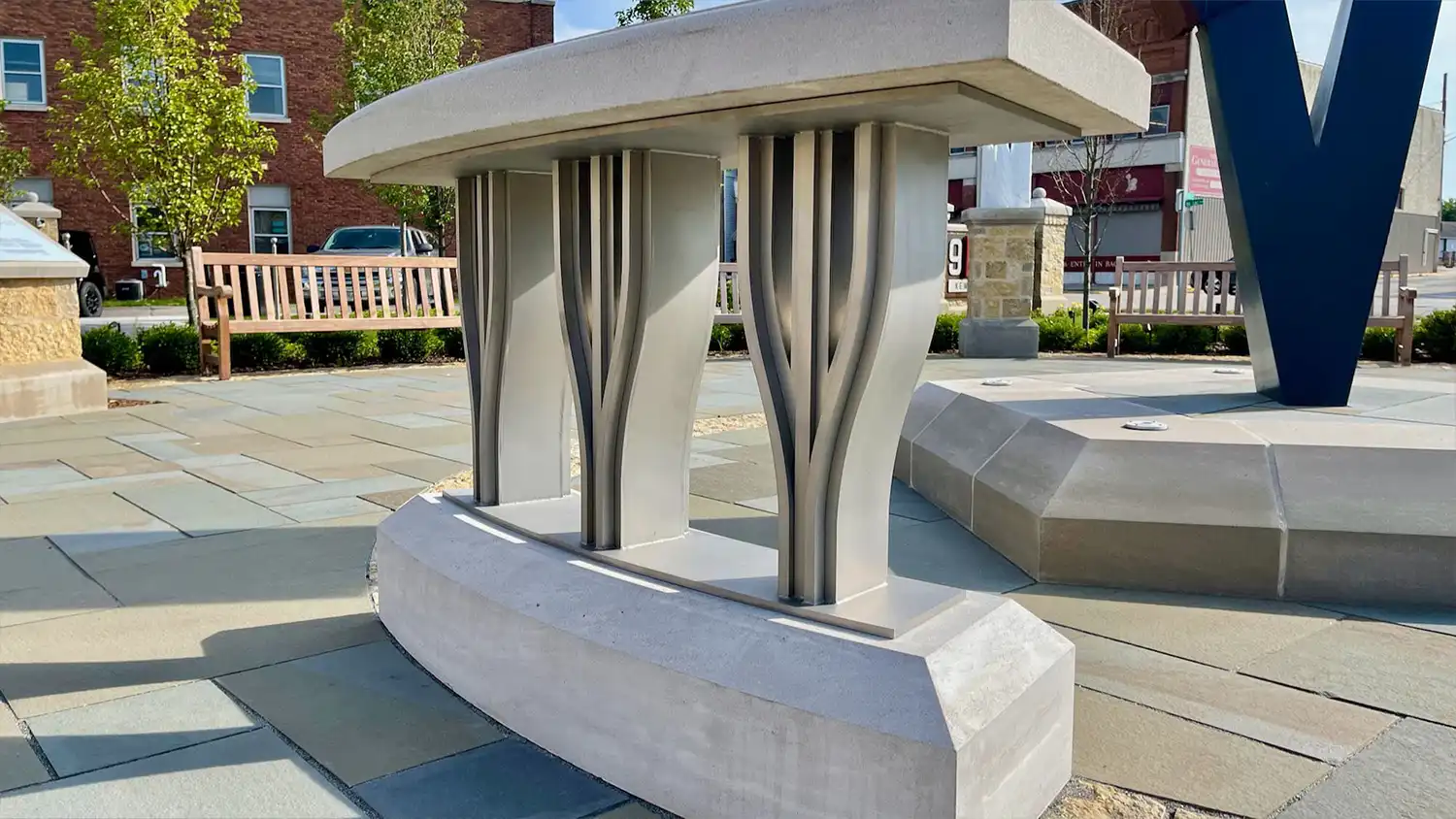 Modern concrete structure with vertical metal elements standing on a paved area with benches nearby.
