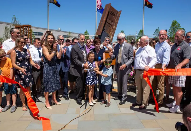 Group of people at an outdoor ribbon-cutting ceremony with two children cutting the ribbon.