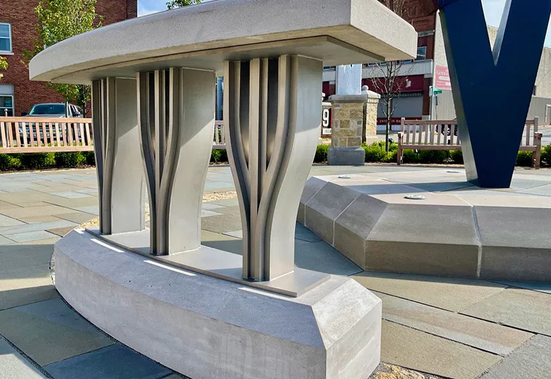 Close-up of curved, modern concrete and metal bench supports in an outdoor plaza with benches and a large sculpture.