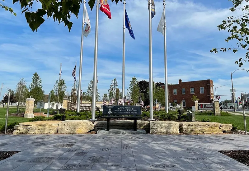 Veterans memorial area with flagpoles, engraved sidewalk, a bench, and small American flags.