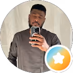 Man wearing a dark shirt taking a selfie in front of a window with sheer curtains.