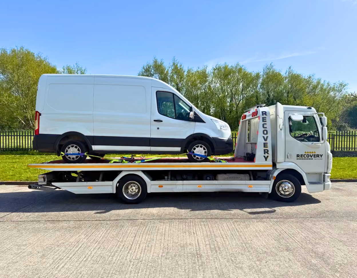 White recovery truck carrying a white van secured on its flatbed under clear blue sky.