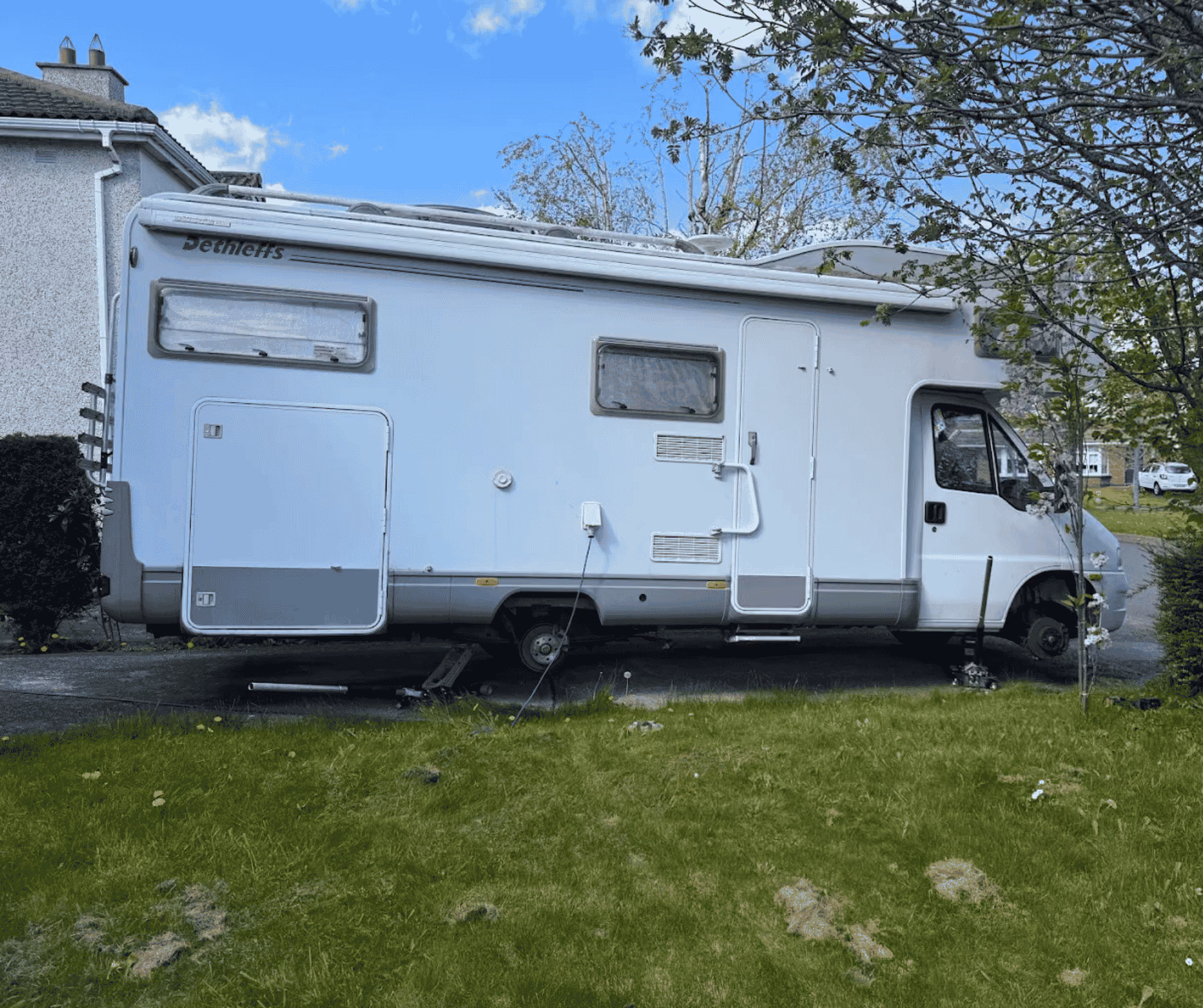 White camper van without wheels parked on driveway with a green lawn in the foreground.