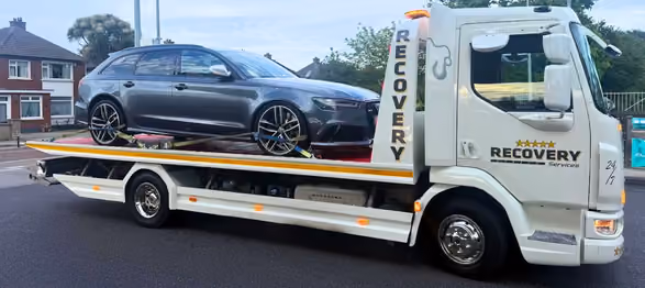 Flatbed recovery truck carrying a grey car parked on a residential street.