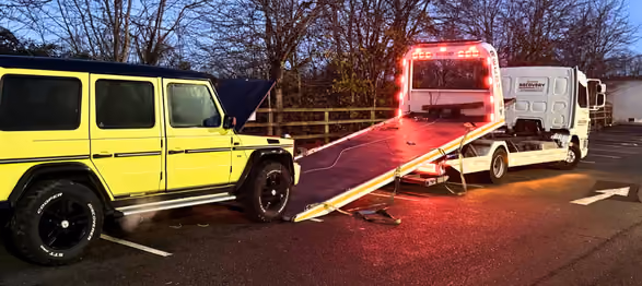 Yellow SUV with open hood parked near a tow truck with red lights and an extended ramp.