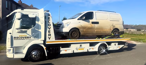 White recovery truck loaded with a dirty white van on its flatbed under a clear blue sky.