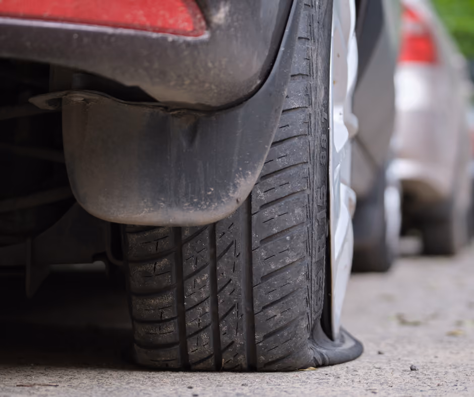 Close-up of a flat tire on a parked car on a paved road.
