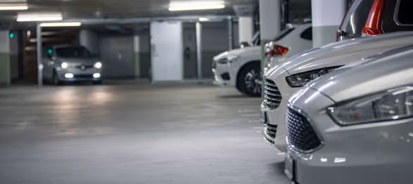Several white and red cars parked in an indoor parking garage with one car approaching in the background.