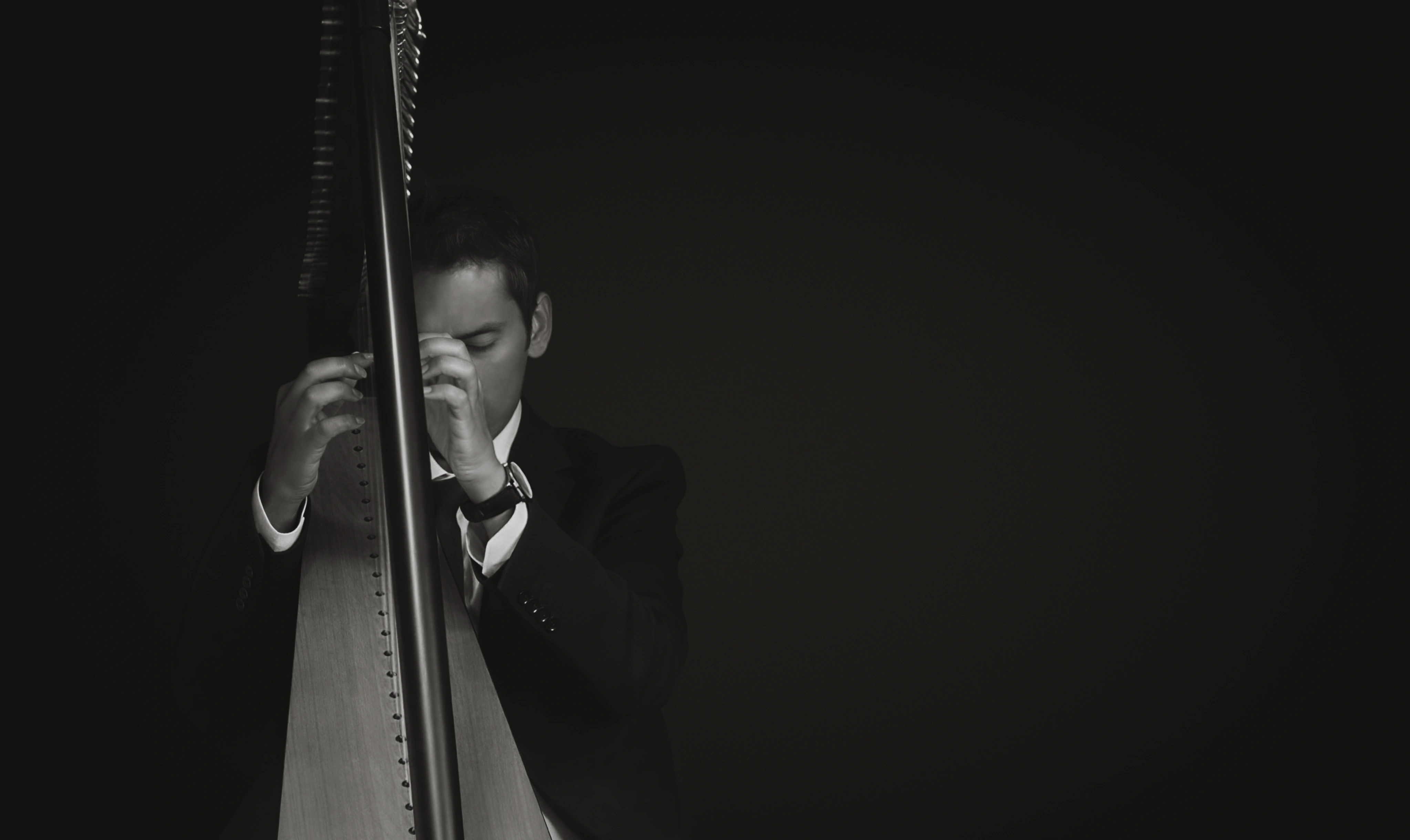 Man plain the harp with eyes closed, shown in black and white with dramatic lighting.