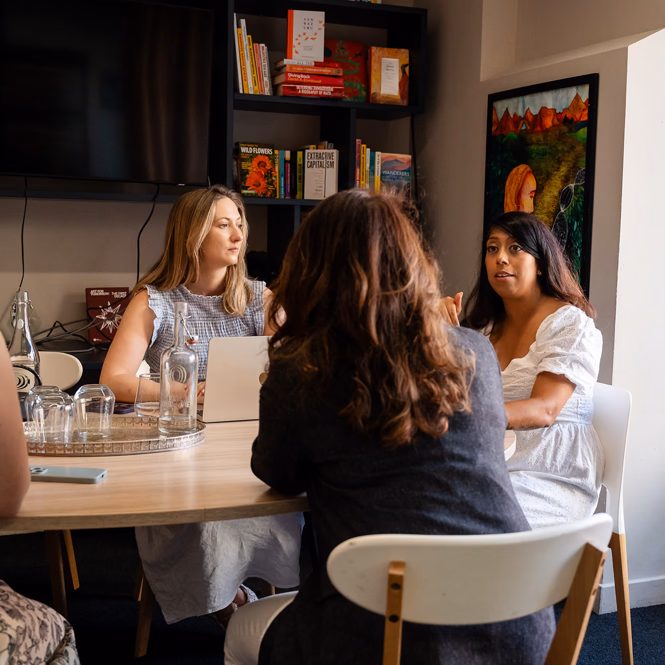 Three women having a meeting in a room with bookshelves and a colorful painting on the wall.