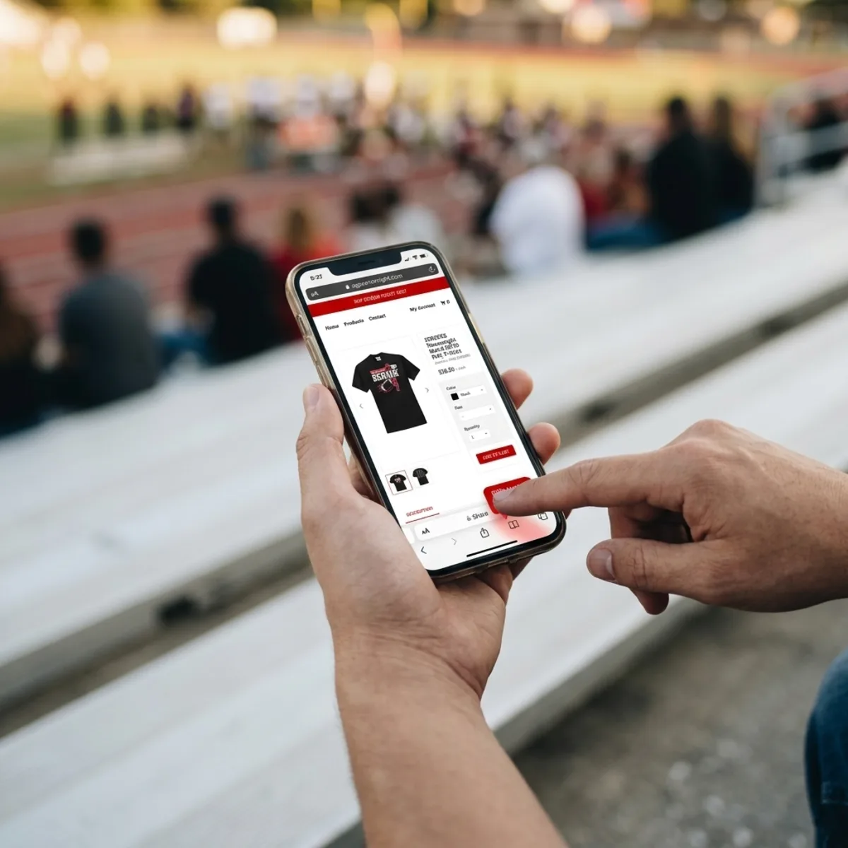 Person browsing a website on a smartphone to purchase a black t-shirt while seated at outdoor bleachers.
