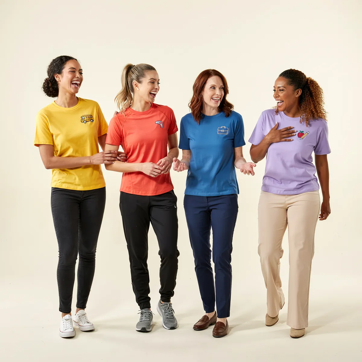 Four women laughing and walking wearing colorful t-shirts with small icons on the chest.