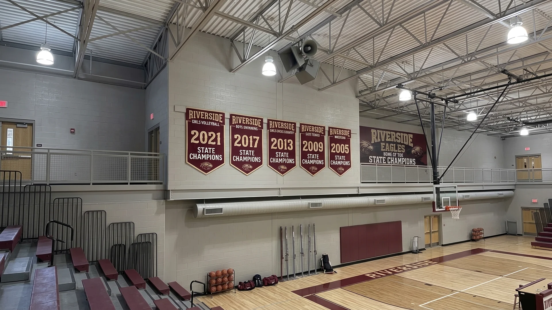 Gymnasium wall with Riverside state champion banners for volleyball, swimming, tennis, and wrestling.