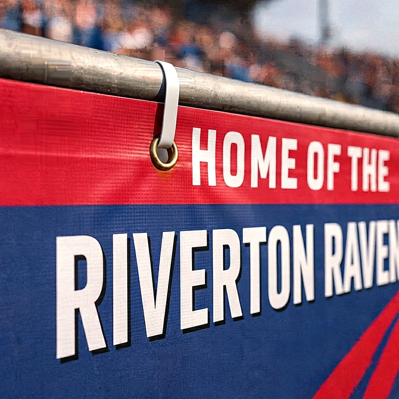 Red and blue banner with large white text reading 'Home of the Riverton Ravens' on a fence.