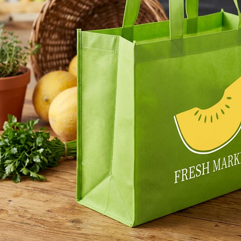 Green reusable grocery bag with a yellow melon slice and 'Fresh Market' text on a wooden table.