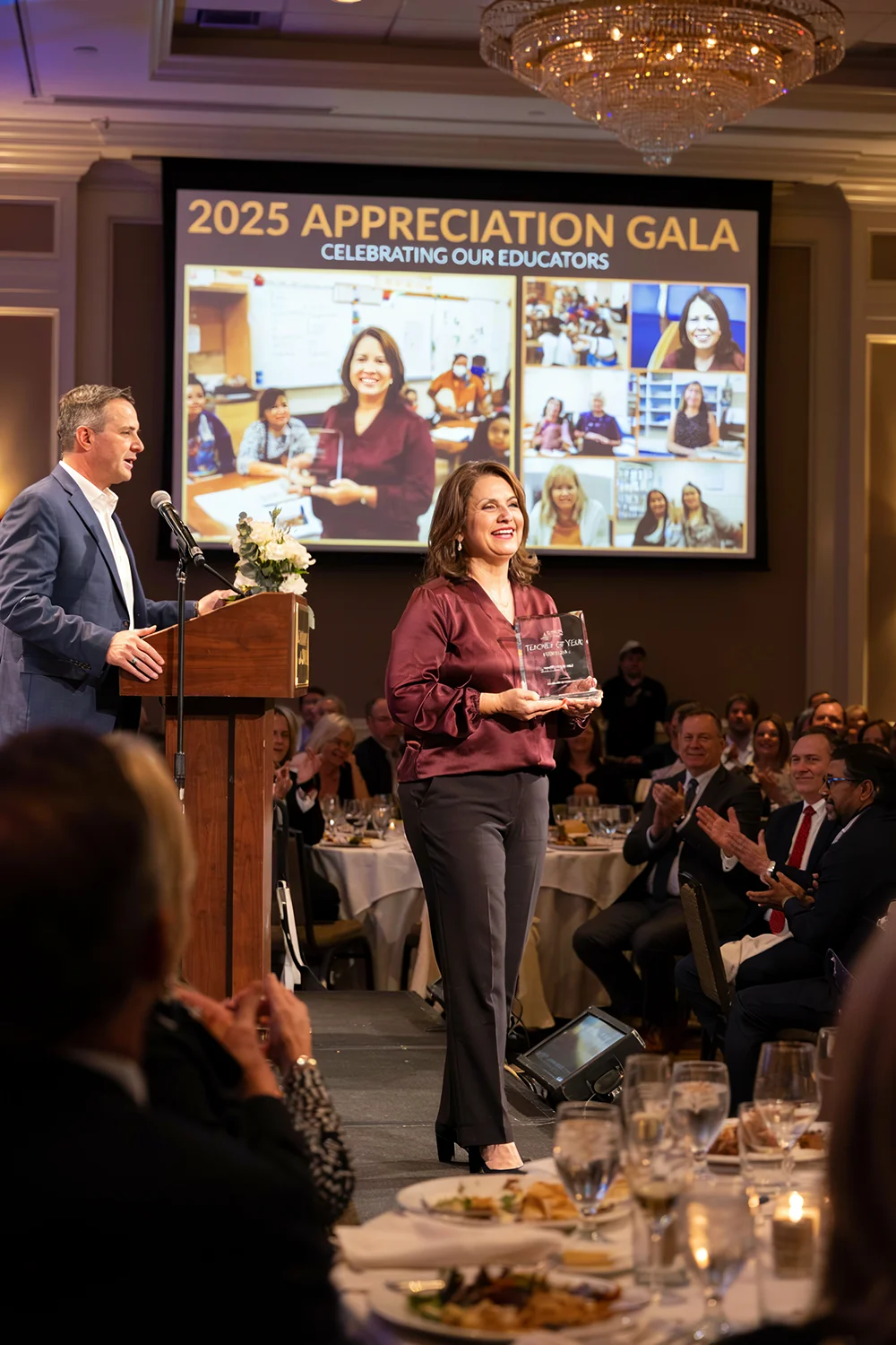 Woman holding an award on stage at the 2025 Appreciation Gala for educators while audience claps.