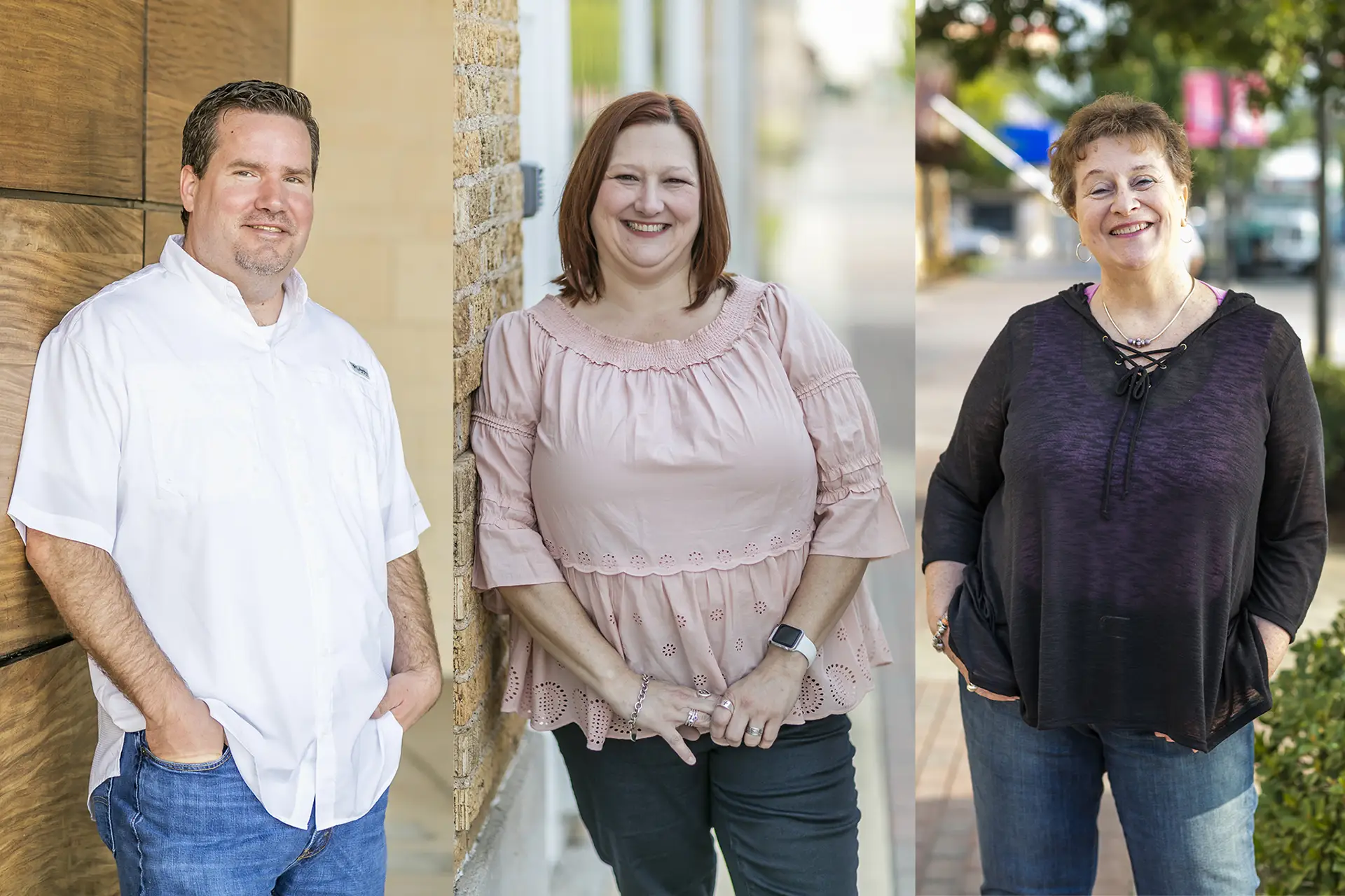 Three team members are standing outdoors smiling, with a wooden wall and street background.