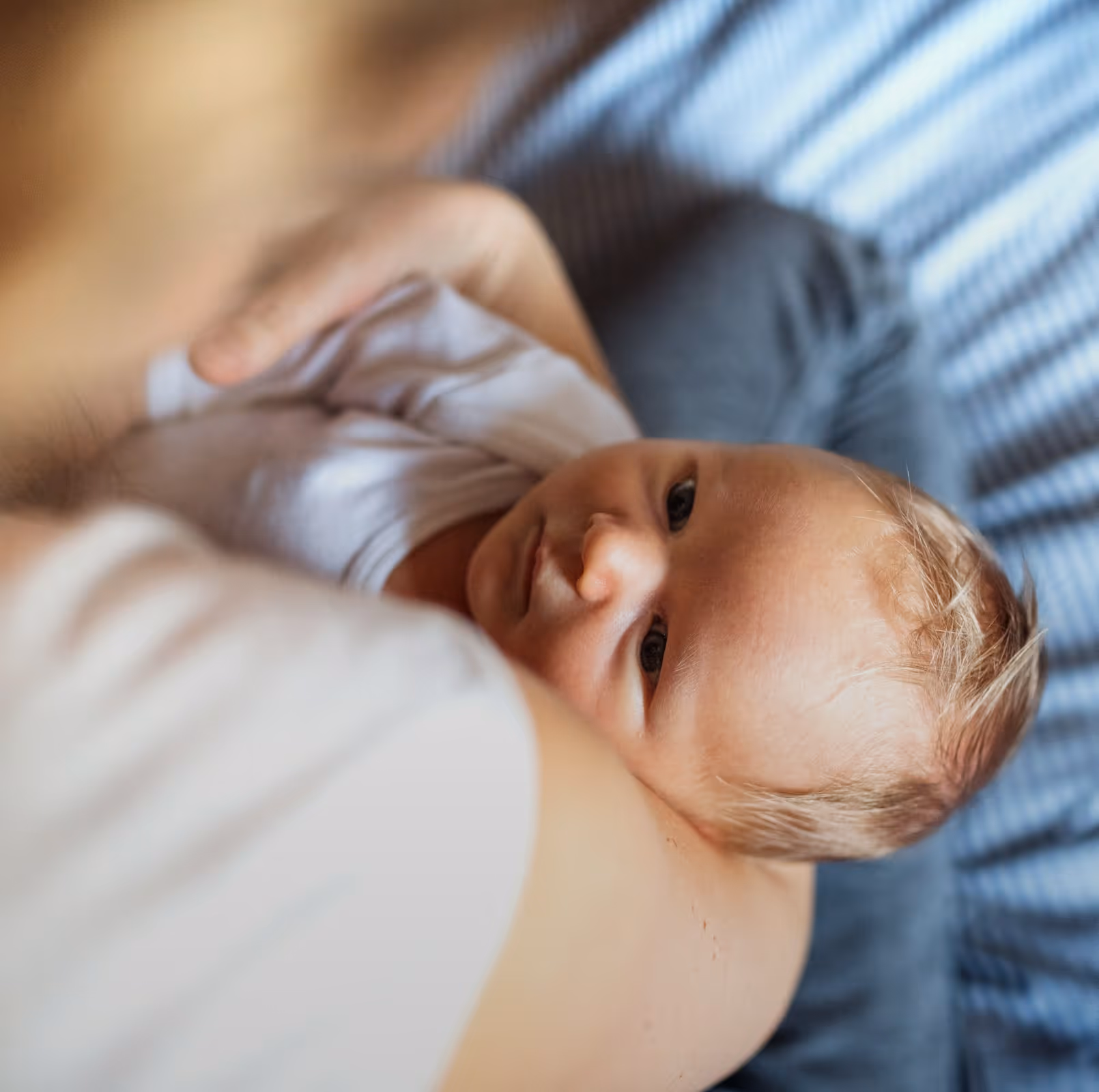 An alert newborn resting against a parent in soft light.