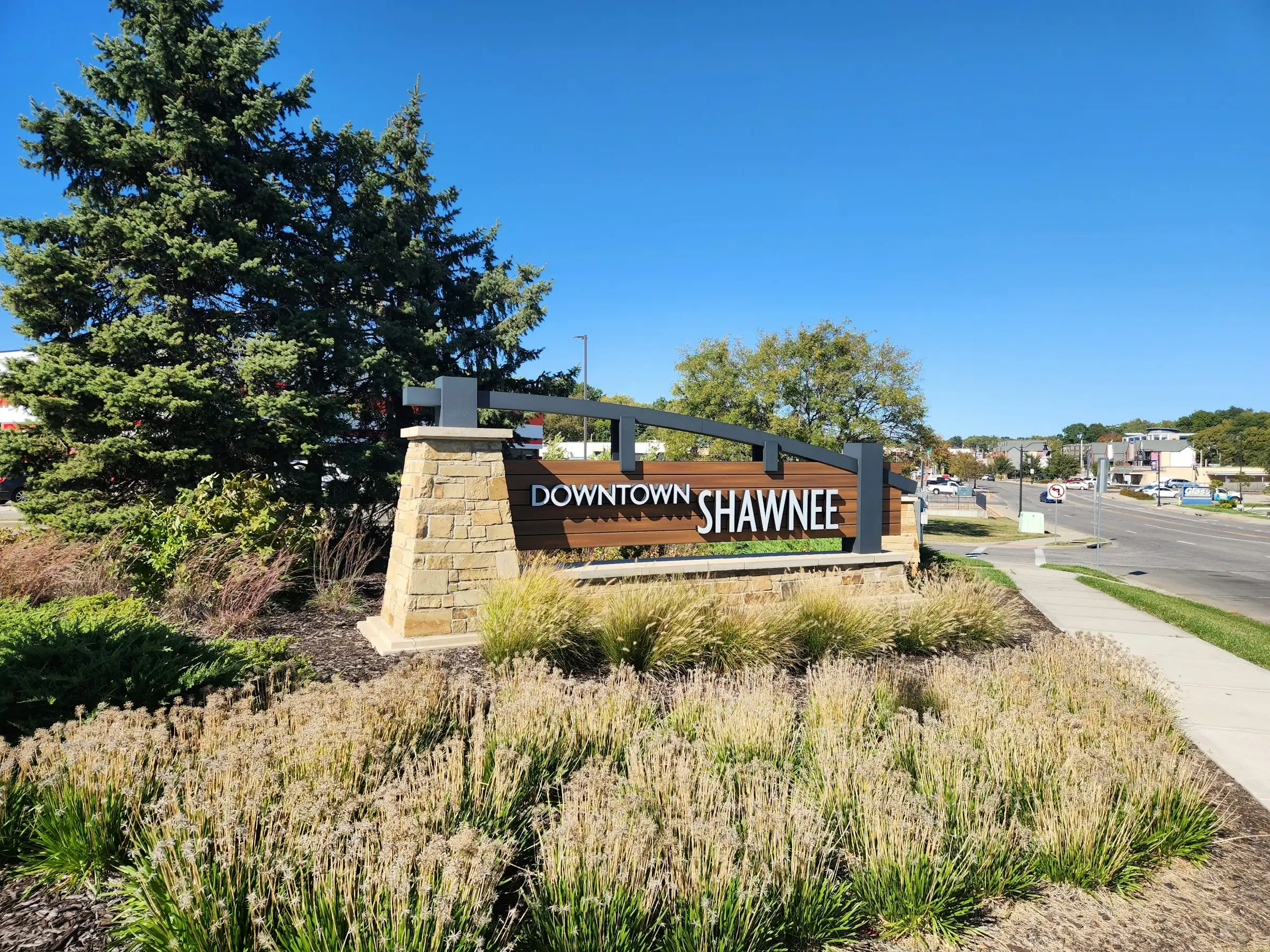 Stone and wood "Downtown Shawnee" monument sign in a landscaped bed beside the street