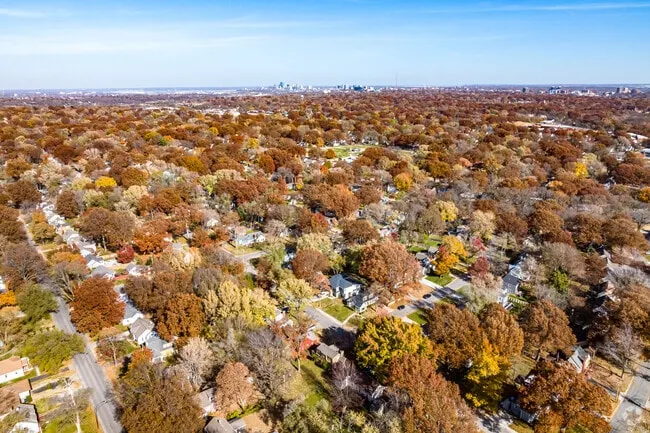 Aerial view of tree-filled Roeland Park, Kansas in autumn with the Kansas City skyline beyond