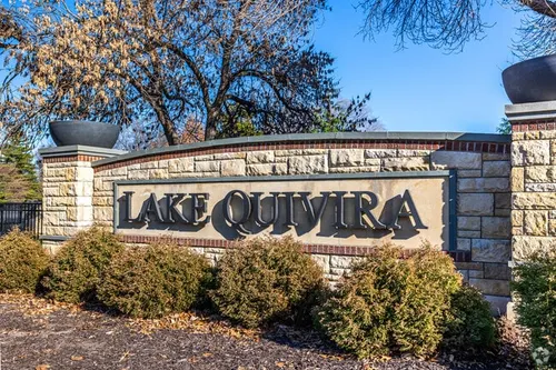 Stone entrance monument lettered LAKE QUIVIRA, framed by low shrubs and bare trees