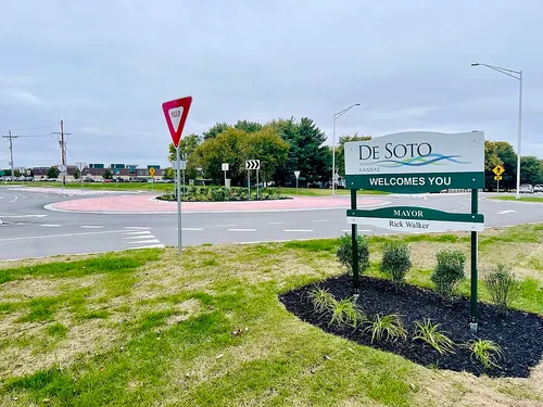 Green "De Soto, Kansas Welcomes You" sign beside a landscaped roundabout at the edge of town