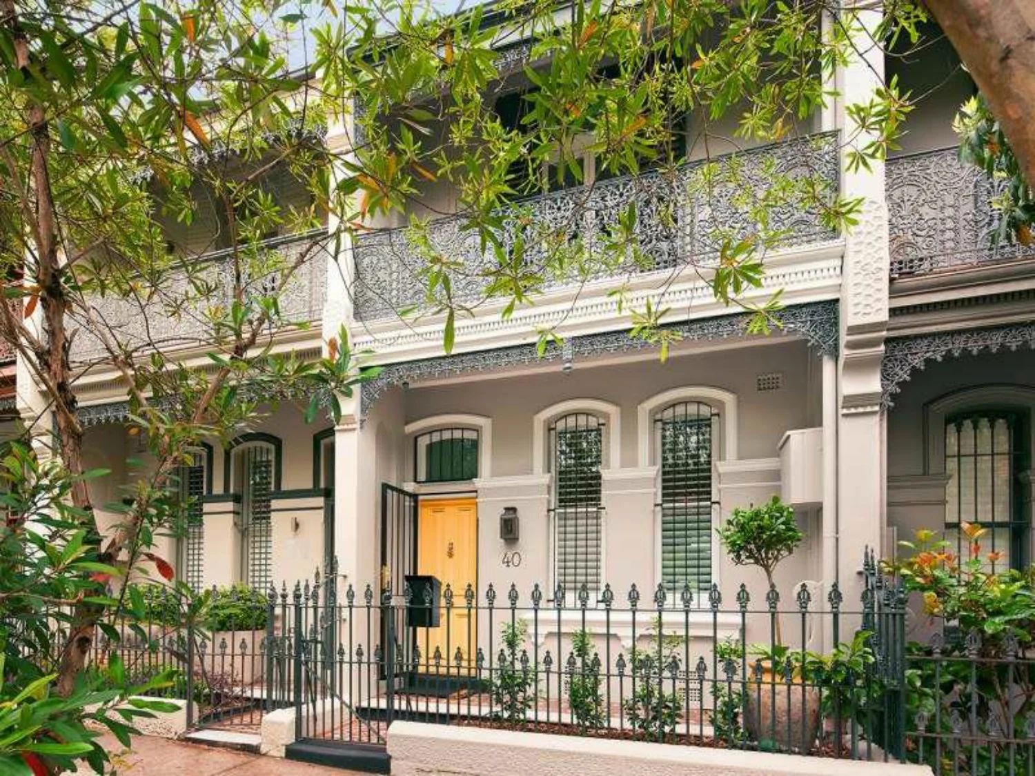 Victorian-style house with gray walls, yellow door, ornate iron balcony, and black wrought iron fence.