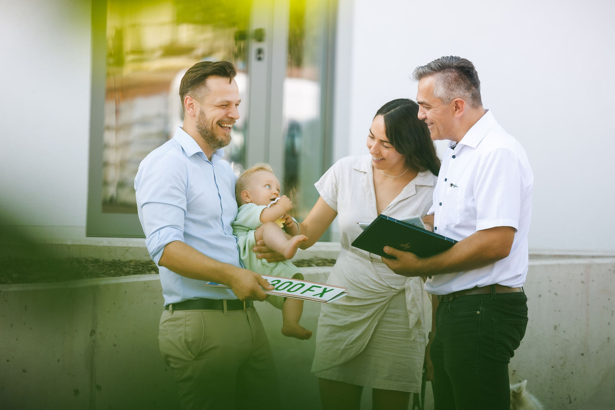 Versicherungsberater spricht mit einer Familie mit Baby über eine KFZ-Anmeldung vor einem Gebäude