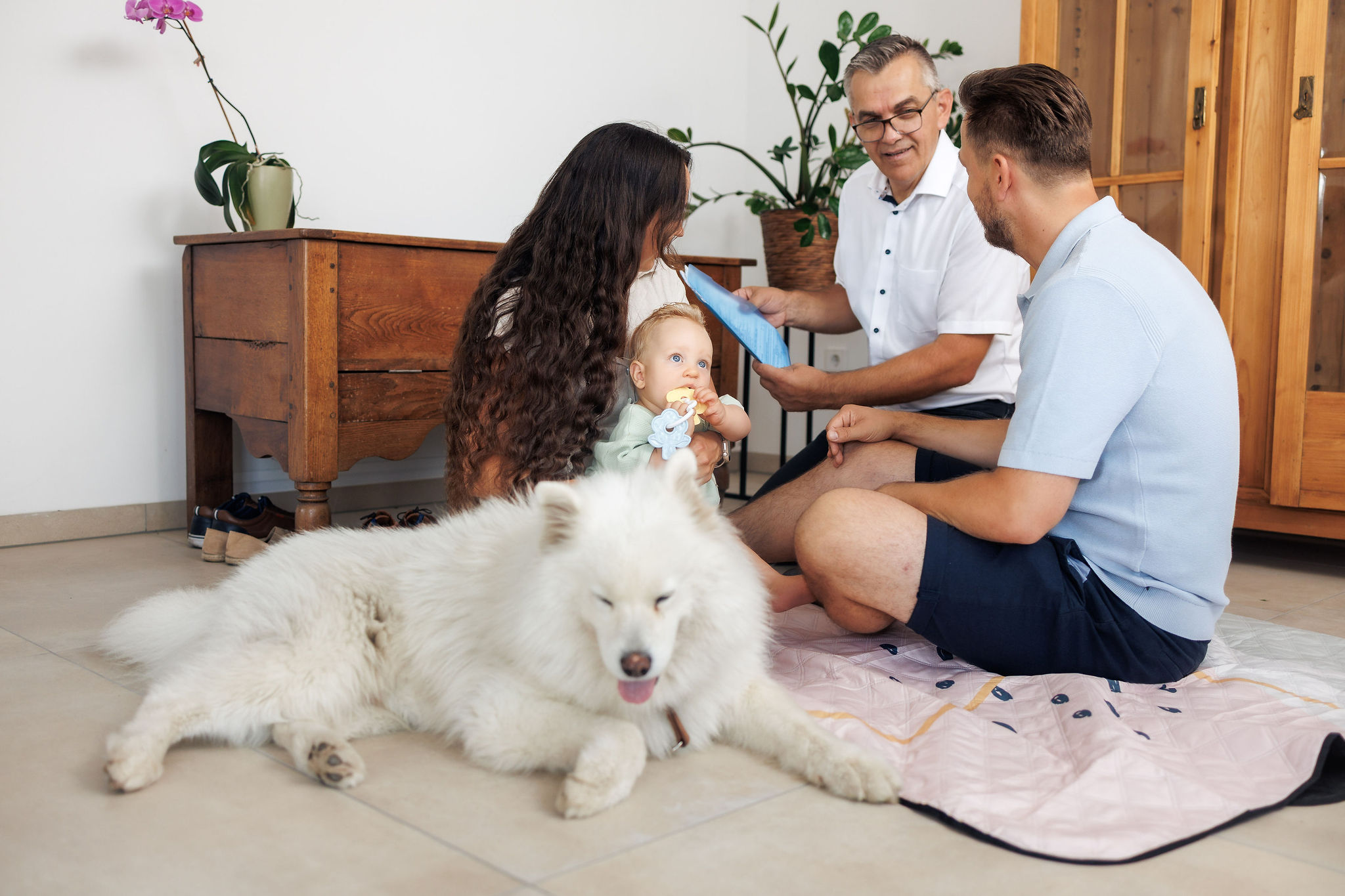 Ein junges Pärchen sitzt mit Baby und Hund am Boden und bespricht mit einem Versicherungsmakler, Versicherungen