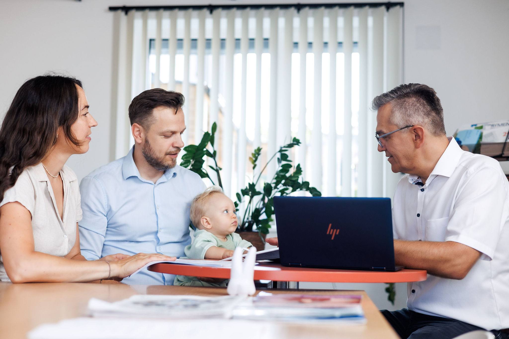 Drei Erwachsenen sitzen mit einem Baby an einem Tisch mit Laptop und besprechen Versicherungs-Themen