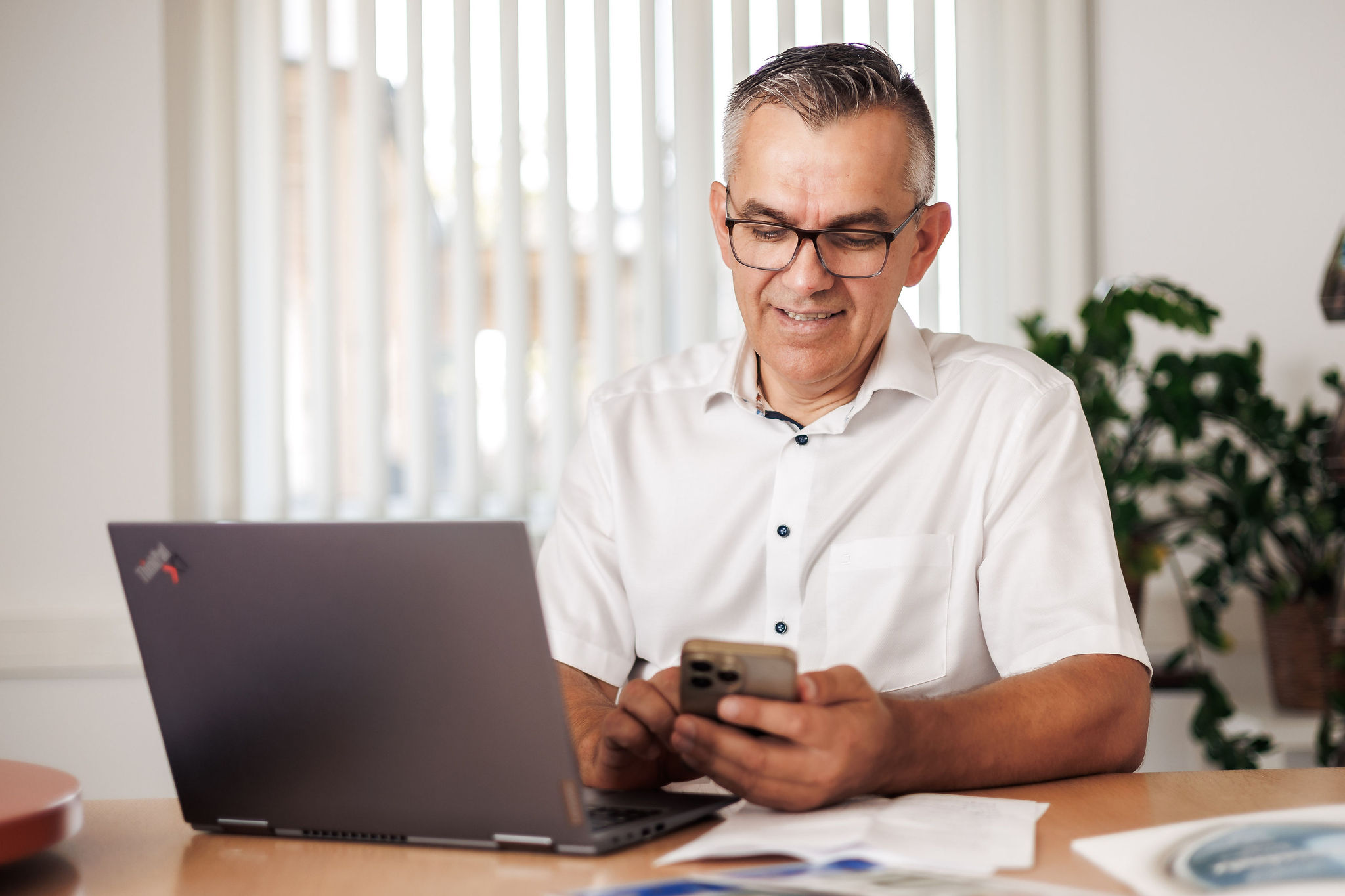 Ein Mann sitzt vor seinem Laptop und schaut auf sein Handy