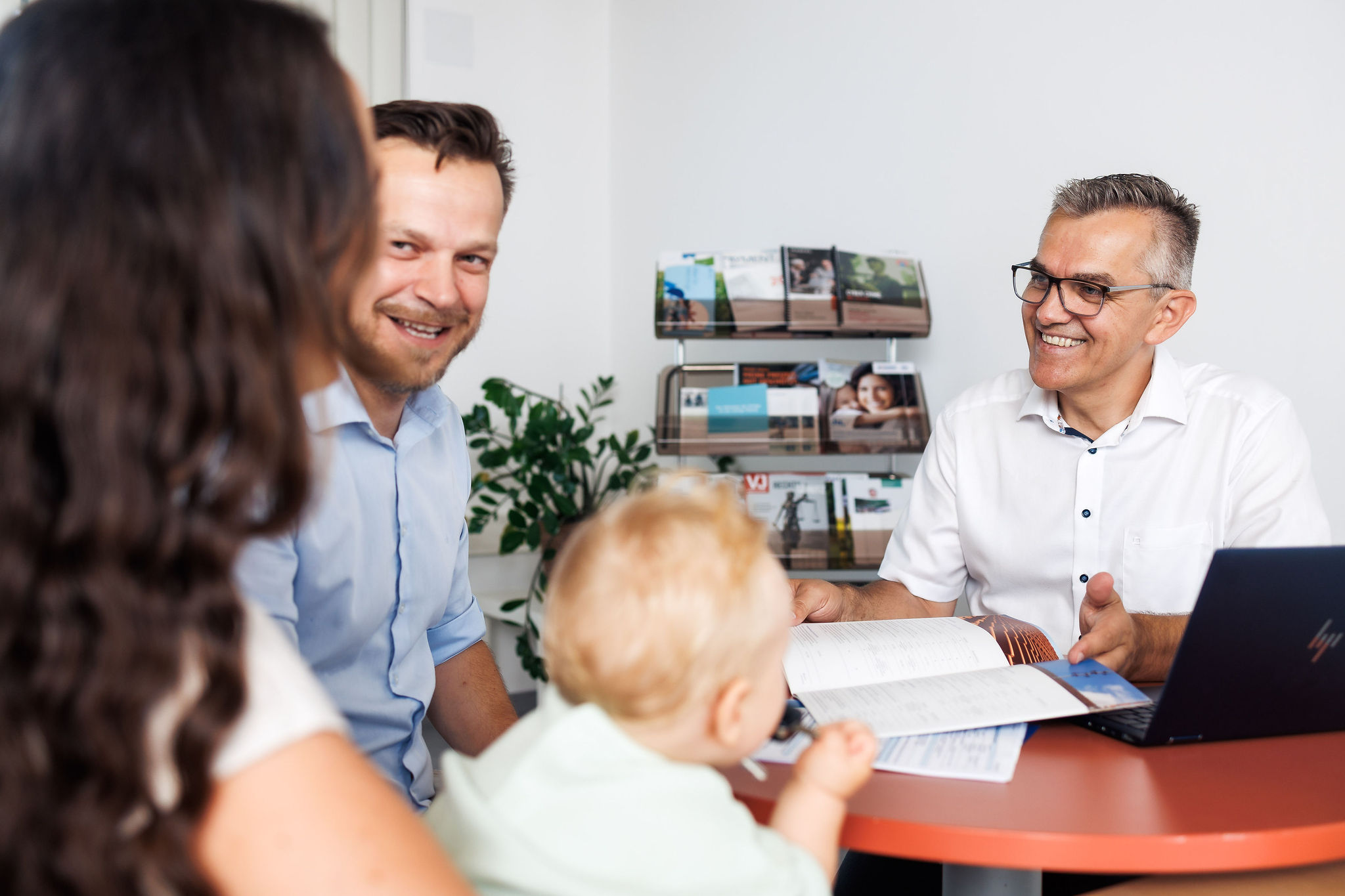 Eine junge Familie sitzt mit Stefan Schöffl an einem Schreibtisch und redet über Versicherungen