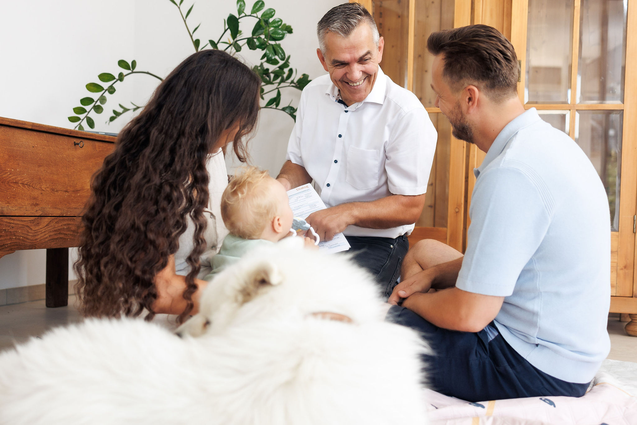 Ein jungen Pärchen sitzt mit Baby und Hund am Boden und spricht mit eine Mann über Versicherungen