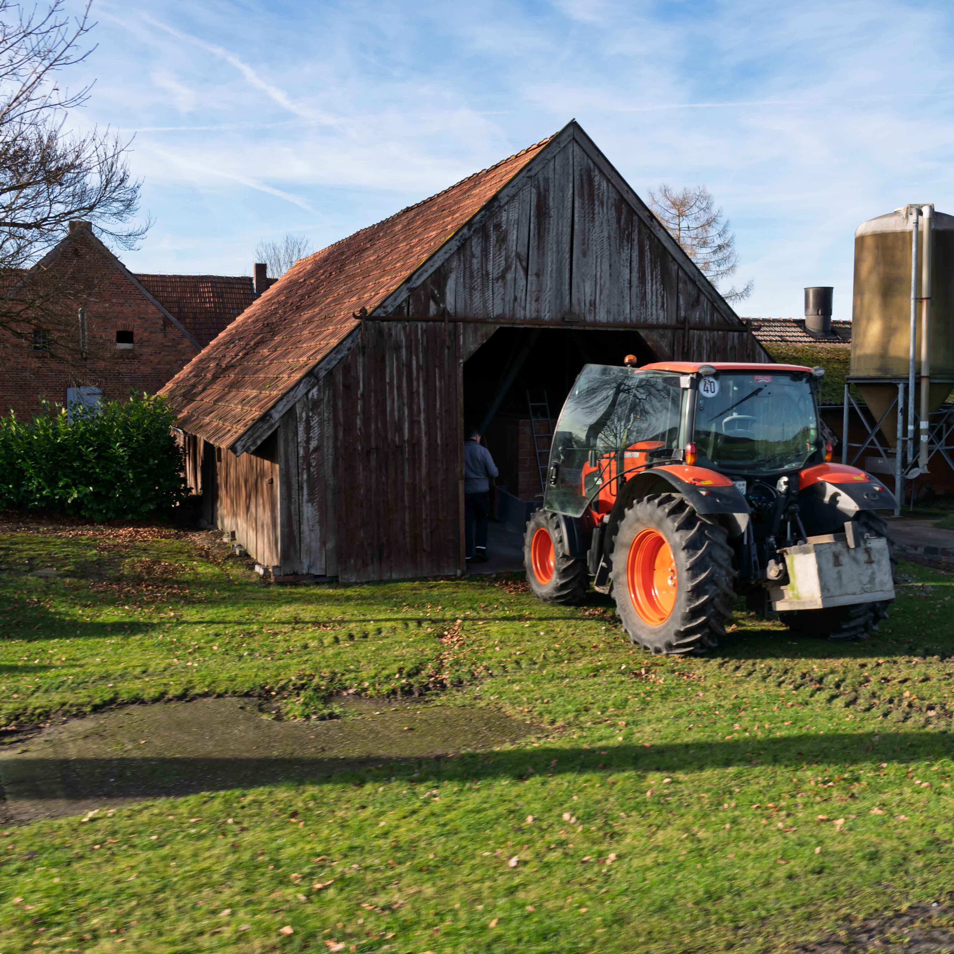 Ein roter Traktor steht vor einer alten Scheune
