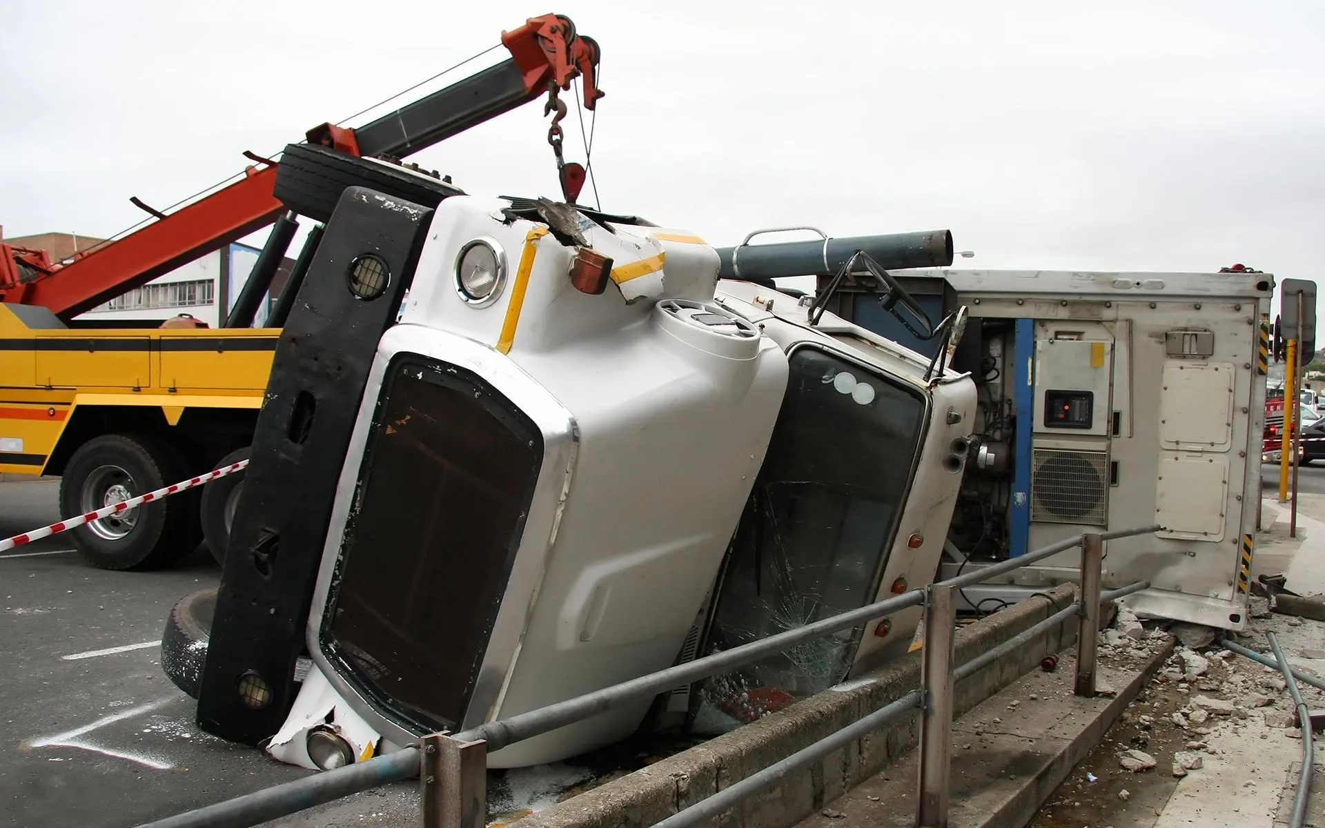 White truck on its side after an accident with yellow tow truck nearby lifting it.