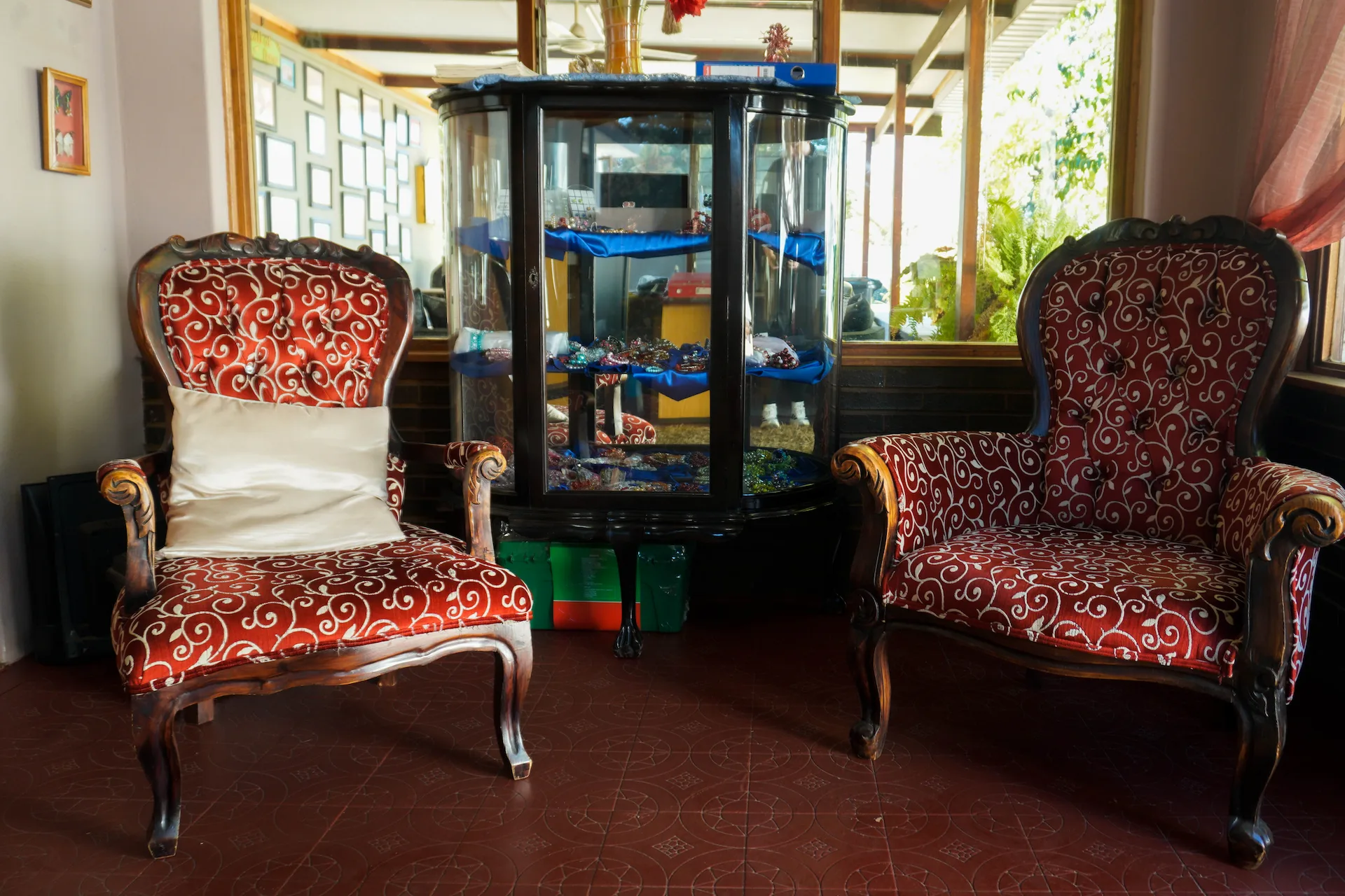 Two vintage red patterned armchairs flanking a glass display cabinet with jewelry inside in the reception area of St. Joseph's GuestHouse