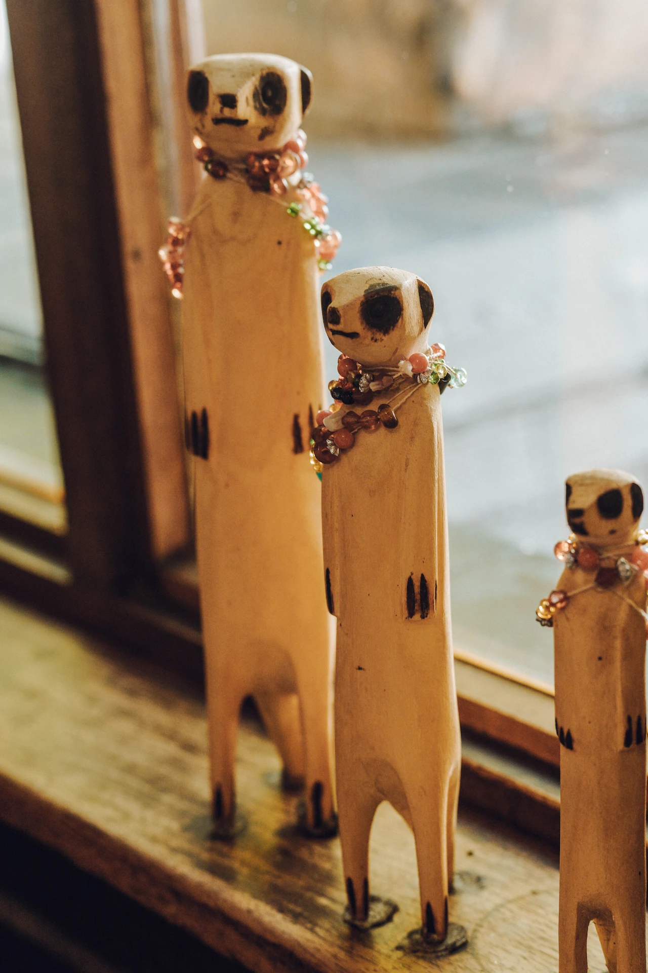 Three wooden meerkat sculptures with bead necklaces standing on a wooden window sill in the reception of St. Joseph's Guest house in Klerksdorp