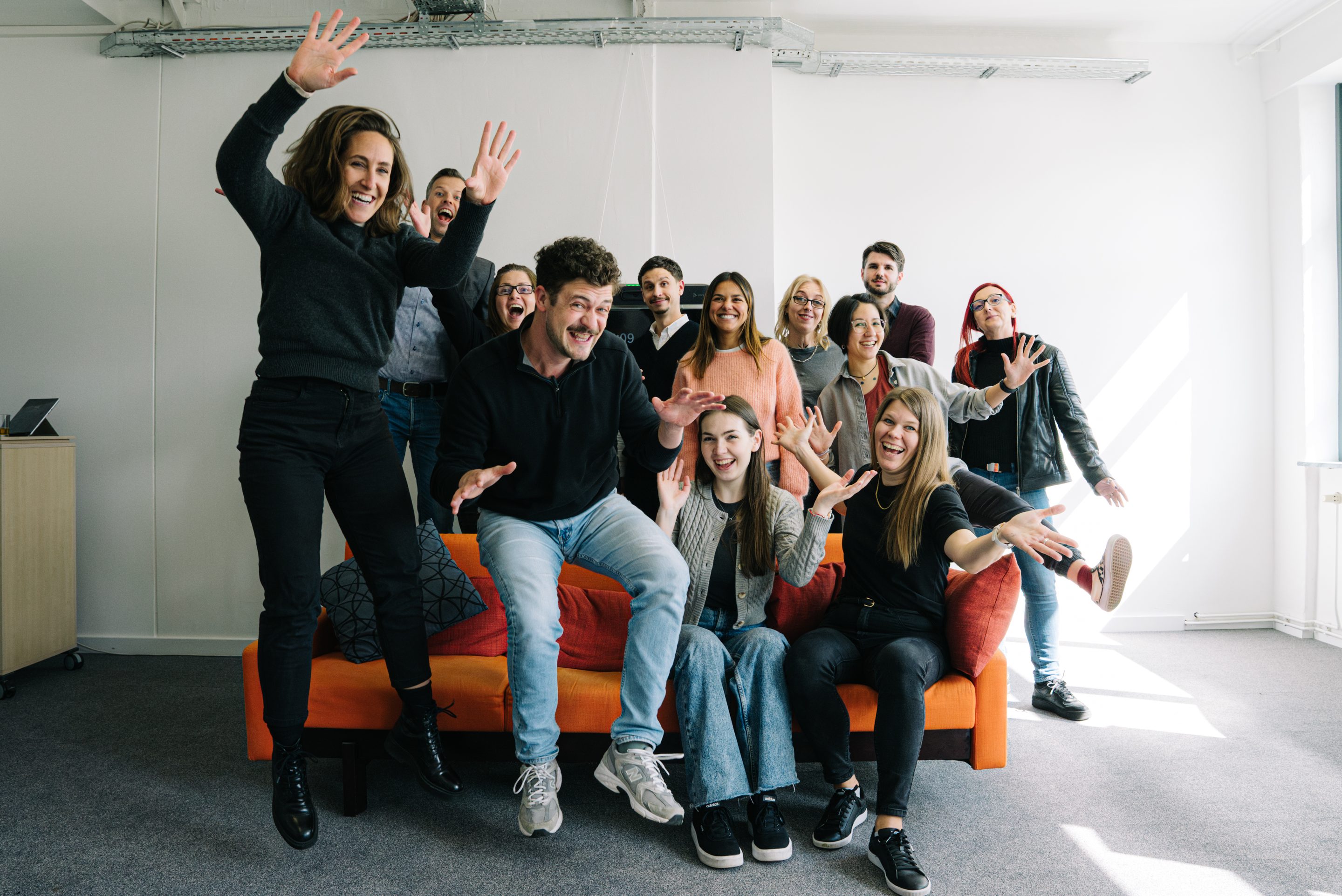 The Emarket team posing playfully and jumping in front of an orange sofa in the office