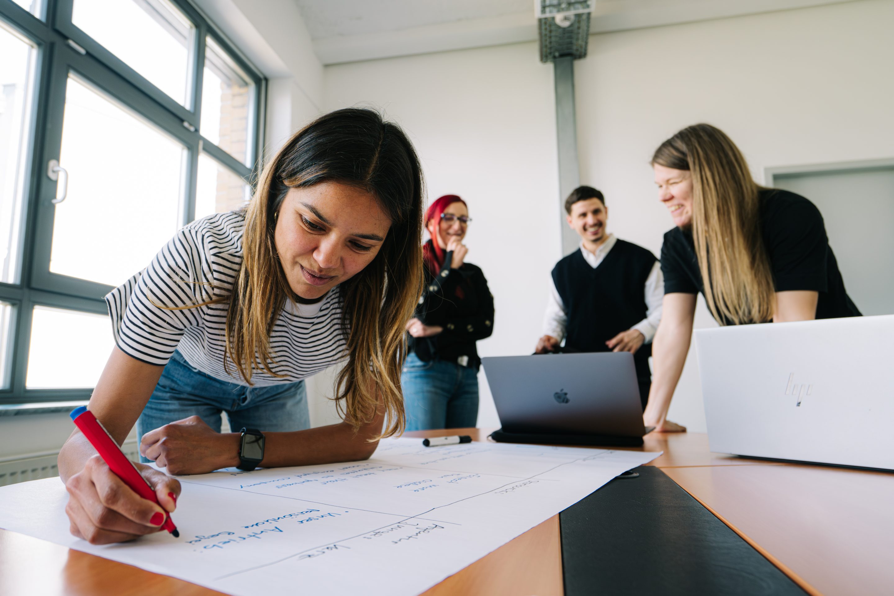An Emarket employee writes ideas on a flipchart while three colleagues look on, laughing